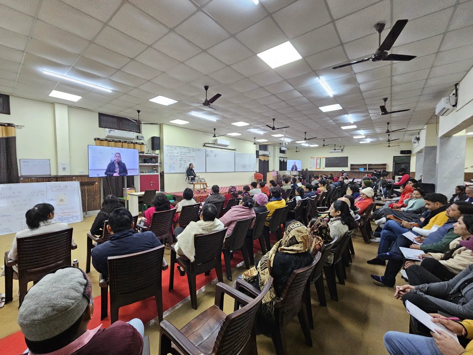 An audience watching a speaker on screen during an educational seminar